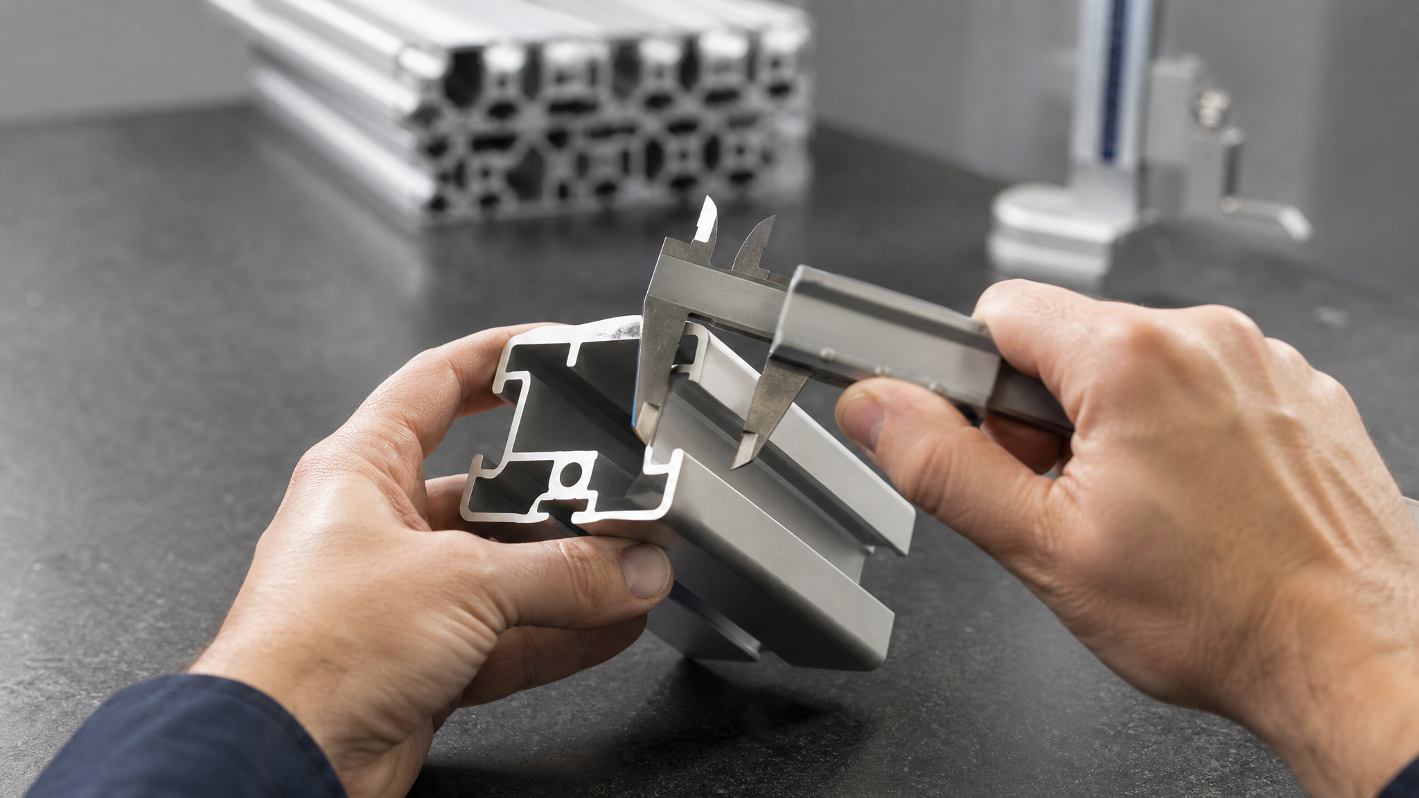 Inspector measuring the wall thickness of an extruded aluminium profile with a vernier caliper on a granite surface plate